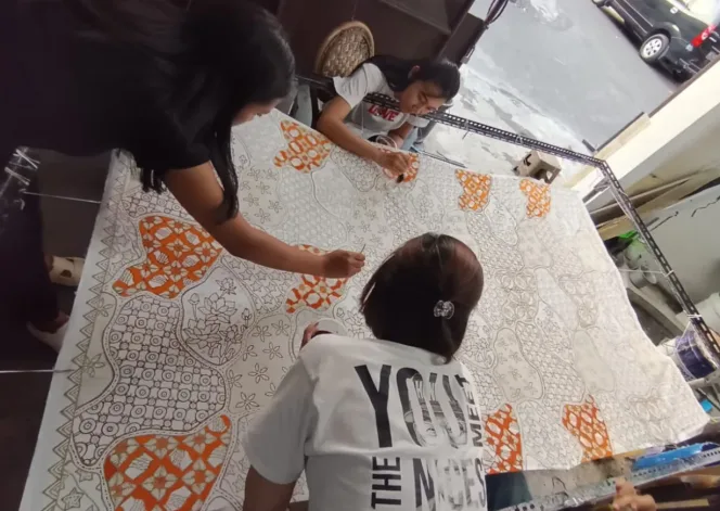 
					Para perajin batik tengah mewarnai batik Malangan dengan tema 
